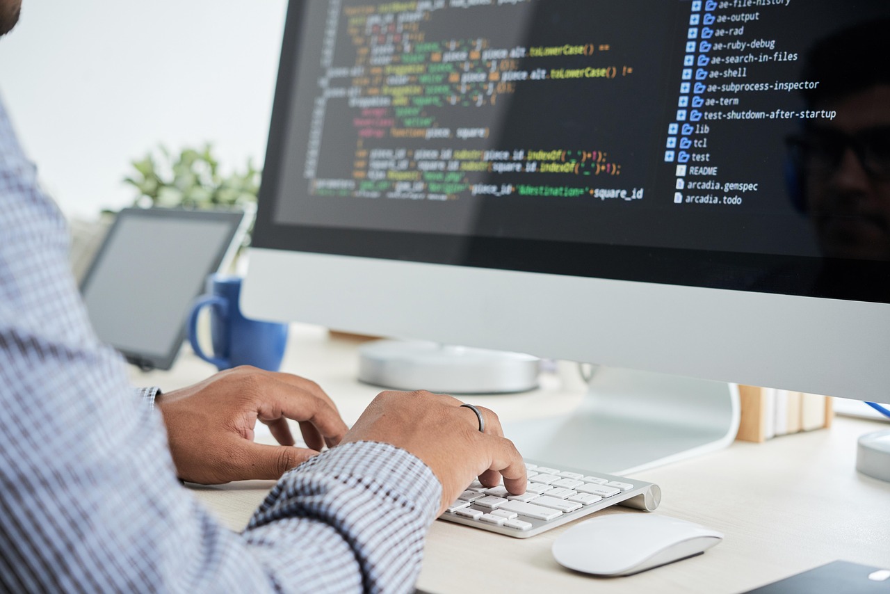 A developer's hands typing on a keyboard with colourful source code on the monitor