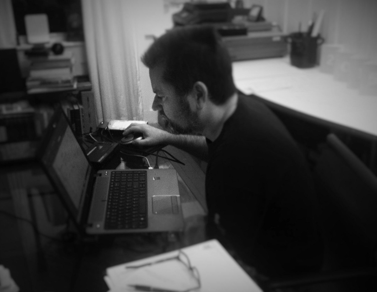 A person working on an HP laptop at a home-office desk, shot in black and white