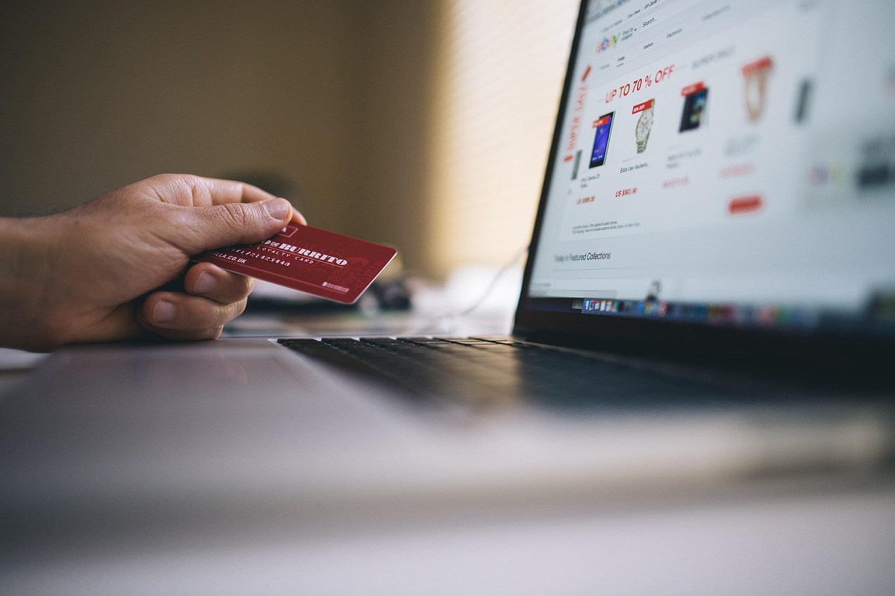 Eine Hand hält eine rote Treuekarte vor einem Laptop, der einen Onlineshop mit Rabatt-Badges anzeigt