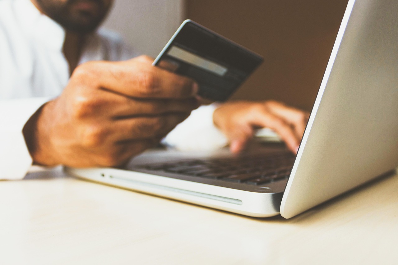 Eine Person hält eine Bankkarte, während sie auf einem Laptop tippt und eine Online-Zahlung abschließt