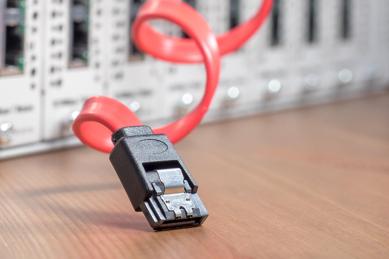 Un conector de cable de datos SATA rojo apoyado sobre un escritorio frente a las bahías de hardware de un servidor
