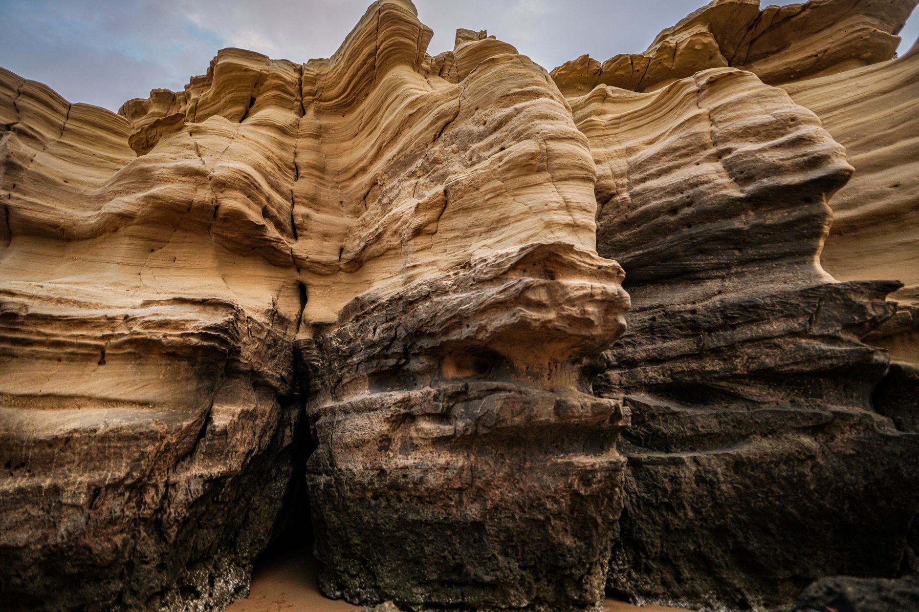 A sandstone cliff face showing horizontal layers stacked one above another, pale bands over darker rock