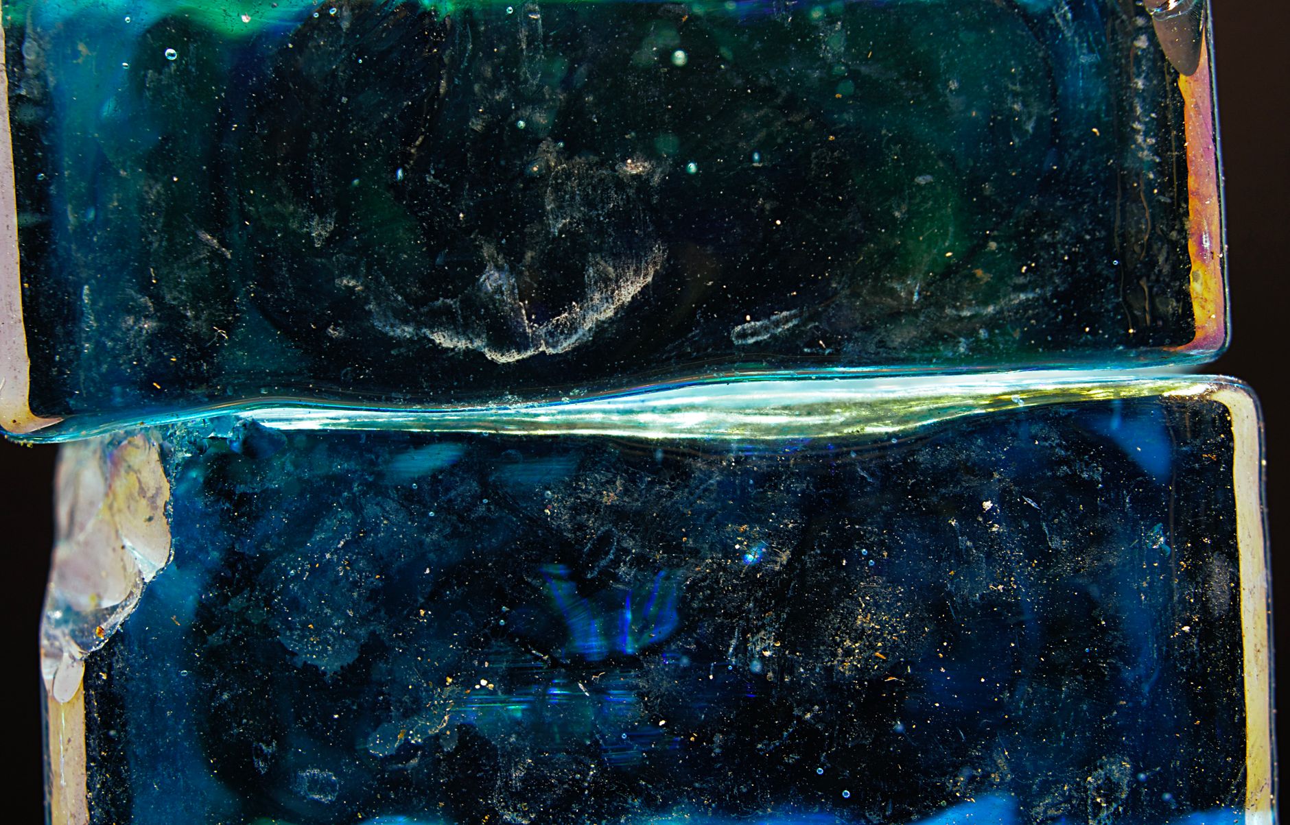 Two blocks of blue-green glass stacked one on the other, an iridescent seam running along the join