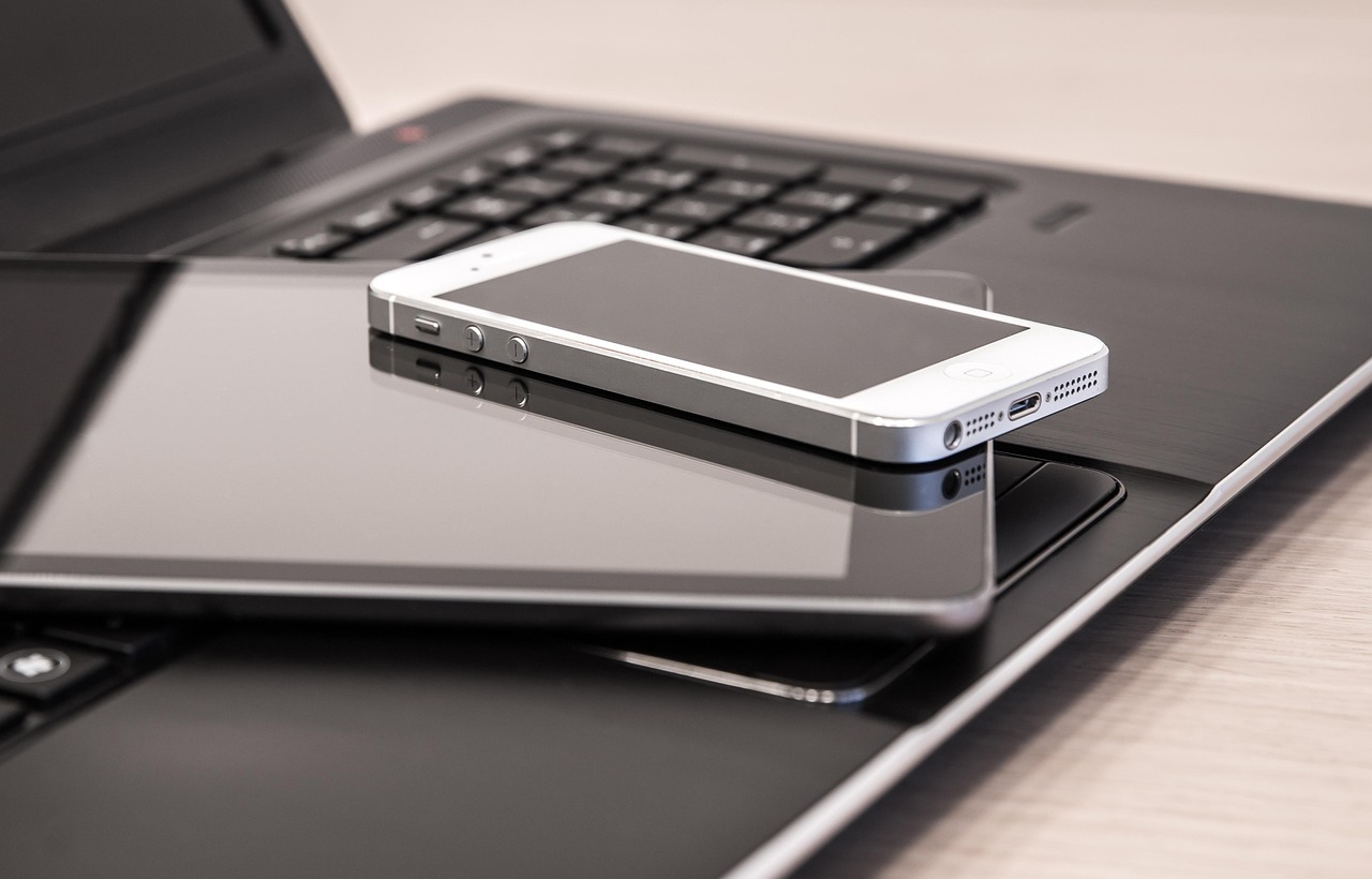 Un smartphone posé sur une tablette et un portable, trois écrans de tailles différentes