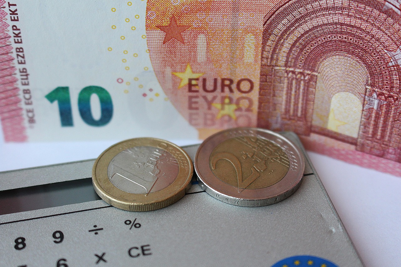 A calculator resting on euro coins and a banknote, used to work out a monthly budget
