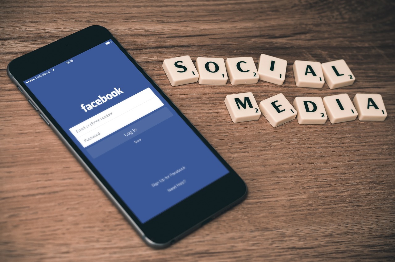 Un smartphone mostrando la pantalla de inicio de sesión de Facebook junto a fichas de Scrabble que forman las palabras SOCIAL MEDIA