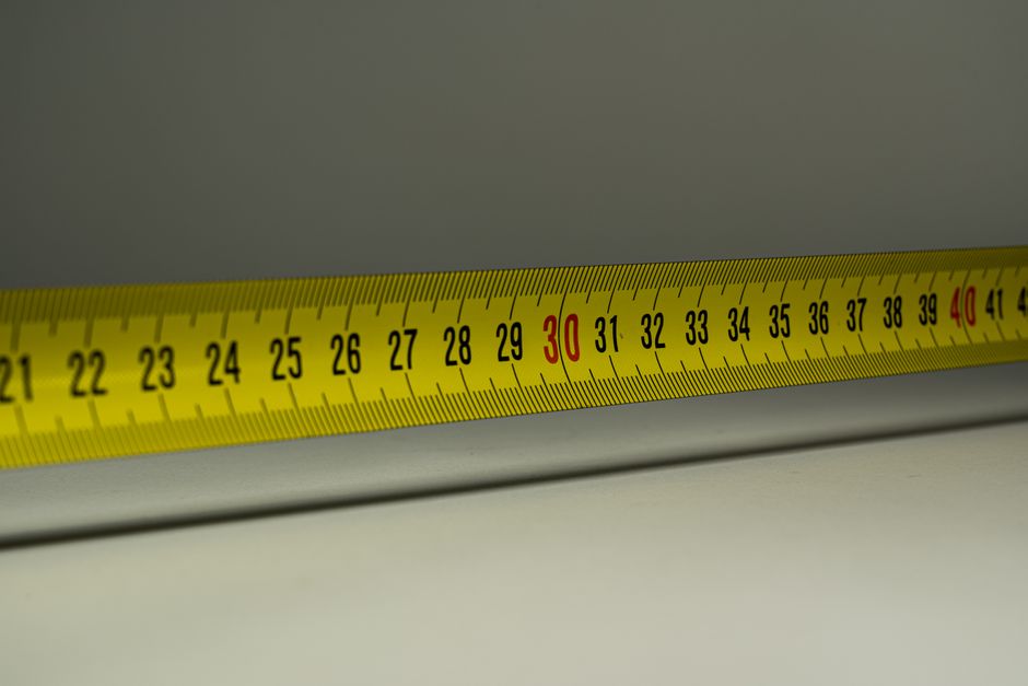 A yellow tape measure stretched diagonally across a grey background, graduations from 21 to 42 with 30 and 40 printed in red