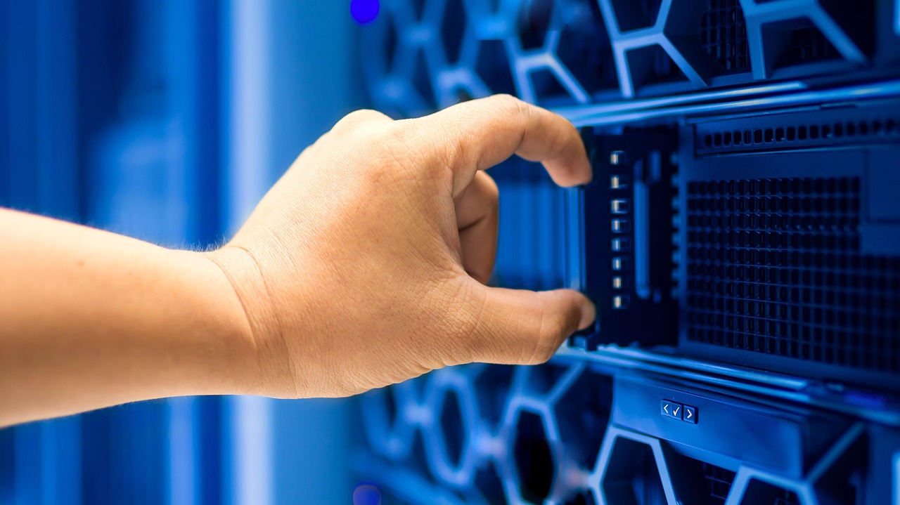 La main d'un technicien manipulant un serveur éclairé en bleu dans une baie de datacenter