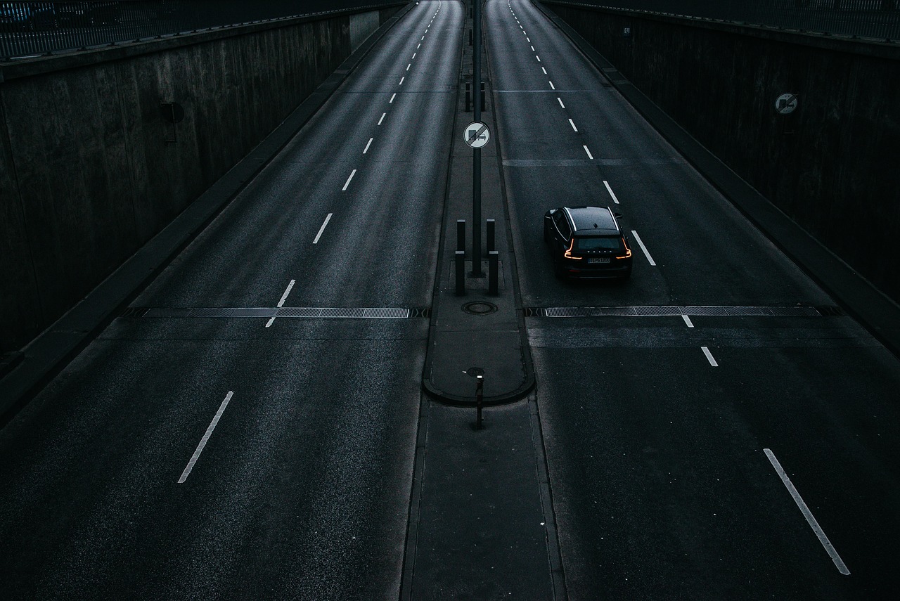 A dual carriageway seen from above, split by a central reservation, with a single dark car on the right-hand side